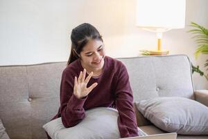 ontspannen jong Aziatisch vrouw genieten van ontspanning Aan een comfortabel sofa Bij huis. de mooi meisje rustig ontspant en ademt vers lucht in de huis. kijk maar films en sociaal netwerken. foto