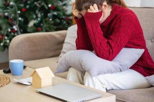 een jong Aziatisch vrouw zit Aan een sofa in haar huis, gevoel bezorgd en gefrustreerd over haar maandelijks uitgaven. divers nut rekeningen. foto