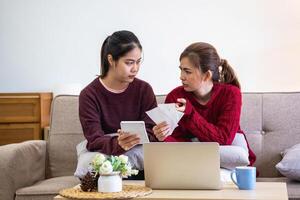 een jong Aziatisch vrouw zit Aan een sofa in haar huis, gevoel bezorgd en gefrustreerd over haar maandelijks uitgaven. divers nut rekeningen. foto