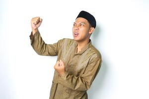 opgewonden Aziatisch moslim Mens vervelend Islamitisch kleren verhogen vuist tonen zege gebaar in eid mubarak viering geïsoleerd Aan wit gebaar foto
