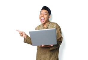 opgewonden Aziatisch moslim Mens Holding laptop richten naar naast en schreeuwen naar camera geïsoleerd Aan wit achtergrond foto