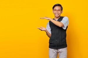 vrolijke aziatische man die product op gele achtergrond toont foto
