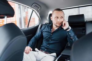 een moderne zakenman spreekt achter in de auto aan de telefoon foto