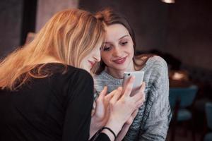 twee meisjes glimlachen en gebruiken een smartphone in een café