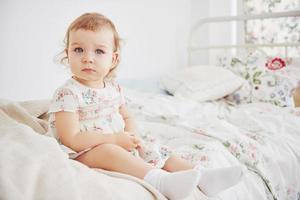 meisje van de baby in schattige jurk aanbrengen op bed spelen met speelgoed door het huis. witte vintage kinderkamer. kindertijd concept foto