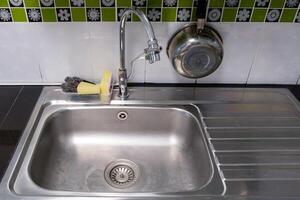 de schone metalen gootsteen met de chromen kraan na het wassen op het moderne aanrecht. foto