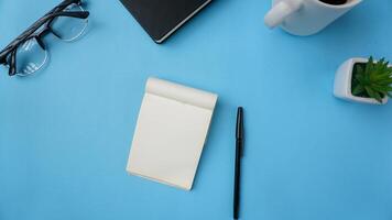 werkruimte bureau met notitieboekjes, pennen, bril, en koffie Aan blauw achtergrond foto