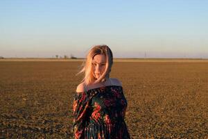 vrouw in een geploegd veld- in een rood Zwart jurk Aan een zonsondergang achtergrond. foto