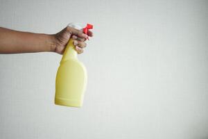Holding een plastic fles sproeien desinfecteren tegen wit muur foto