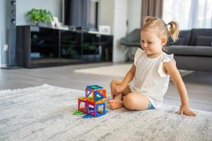 weinig meisje spelen kleurrijk magneet plastic blokken uitrusting Bij huis. de kind spelen leerzaam spellen. vroeg kinderjaren ontwikkeling. foto