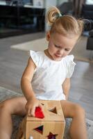 schattig Kaukasisch weinig meisje spelen Aan de verdieping Bij huis met eco houten speelgoed. de kind spelen leerzaam spellen. foto