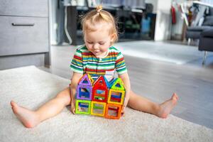 weinig meisje spelen kleurrijk magneet plastic blokken uitrusting Bij huis. de kind spelen leerzaam spellen. vroeg kinderjaren ontwikkeling. foto