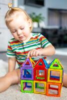 weinig meisje spelen kleurrijk magneet plastic blokken uitrusting Bij huis. de kind spelen leerzaam spellen. vroeg kinderjaren ontwikkeling. foto