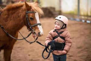 portret van weinig meisje in beschermend jasje en helm met haar bruin pony voordat rijden les foto