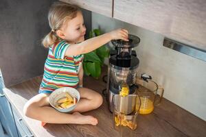 weinig meisje maken vers sap zittend Aan de tafel in huis keuken foto