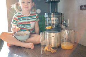 weinig meisje maken vers sap Aan de tafel in huis keuken. focus Aan sapcentrifuge foto