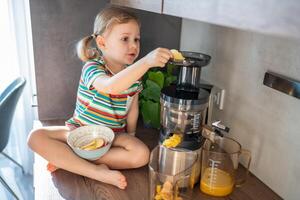 weinig meisje maken vers sap zittend Aan de tafel in huis keuken foto