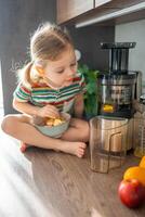 weinig meisje maken vers sap zittend Aan de tafel in huis keuken foto