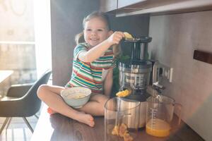 weinig meisje maken vers sap zittend Aan de tafel in huis keuken foto