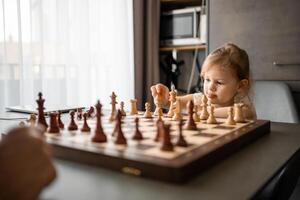 weinig meisje spelen schaak met haar vader Bij de tafel in huis keuken. de concept vroeg kinderjaren ontwikkeling en onderwijs. familie vrije tijd, communicatie en recreatie. foto