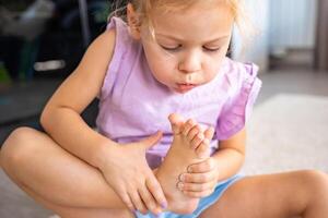 weinig meisje aan het doen pedicure en schilderij nagels met kleurrijk roze, blauw en Purper nagel Pools Bij huis. kind meisje blazen Aan uw nagels naar droog de Pools. foto