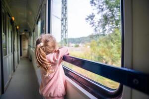 weinig meisje op zoek uit trein venster buiten, terwijl het in beweging. op reis door spoorweg, Europa foto