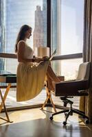 elegant zakenvrouw freelancer werken met laptop en zittend Aan tafel met panoramisch visie in stad achtergrond. laag sleutel foto