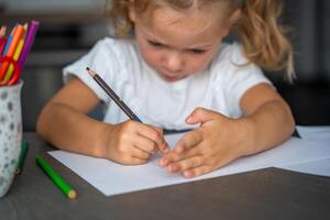 weinig meisje trekt met gekleurde potloden in huis. foto
