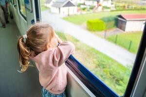 mooi weinig meisje op zoek uit trein venster buiten, gedurende reizend. op reis door spoorweg in Europa foto