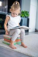 weinig meisje is zittend Aan stack van kinderen boeken en bladeren door een boek met fee verhalen foto