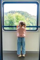 weinig meisje op zoek uit trein venster buiten, terwijl het in beweging. op reis door spoorweg in Europa foto