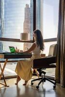 elegant zakenvrouw freelancer werken met laptop en zittend Aan de stoel, genieten van panoramisch visie in de stad achtergrond. laag sleutel foto. hoog kwaliteit foto