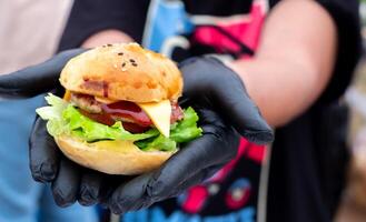 hambuger mini, professioneel hand- chef Holding vers heerlijk en smakelijk handgemaakt hamburger, gegarneerd met salade, tomaten, en komkommer in een detailopname schot, snel voedsel voor uw snel levensstijl foto