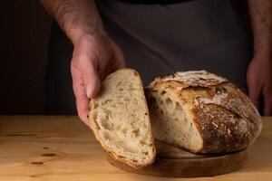 de handen van een jong Mens behandeling zuurdesem brood, markeren de brood met mooi gouden tonen tegen de donker achtergrond. foto