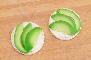 rijst- taart boterhammen met vers avocado en room kaas Aan bamboe snijdend bord. gemakkelijk ontbijt. eetpatroon voedsel. snel en gezond boterhammen. knäckebröd met smakelijk vulling. gezond dieet tussendoortje foto