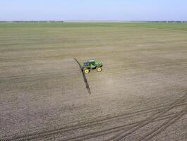 trekker met scharnierend systeem van sproeien pesticiden. bemesting met een tractor, in de het formulier van een aërosol, Aan de veld- van winter tarwe. foto