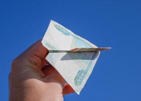 denominaties van Russisch geld, gevouwen in de vliegtuig tegen de blauw lucht in hand- foto