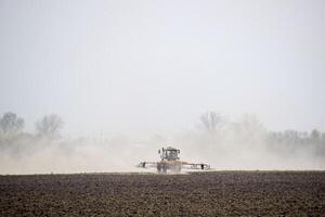 de trekker eggen de bodem Aan de veld- en creëert een wolk van stof achter het foto