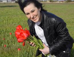 mooi fee jong meisje in een veld- tussen de bloemen van tulpen. portret van een meisje Aan een achtergrond van rood bloemen en een groen veld. veld- van tulpen foto