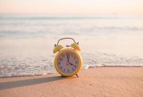 geel alarm klok Aan de strand in de zonsondergang tijd. de concept over tijd naar zomer, reis, vakantie en ontspanning foto