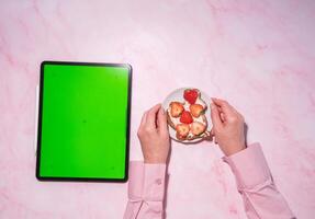 vrouw Holding zacht kaas en aardbei belegd broodje in de buurt groen scherm tablet foto