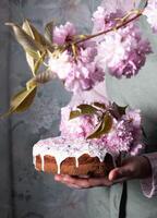 een vrouw siert een eigengemaakt Pasen taart met roze sakura bloemen, lente bloesem foto