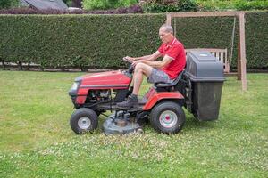 gazon maaier maait de gras, een middelbare leeftijd mannetje tuinman werken Aan een mini trekker foto