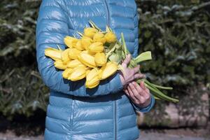 vrouw in een blauw jasje met een boeket van geel voorjaar tulpen, moeder dag geschenk foto