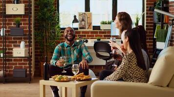 het beste vrienden lachend samen, genieten van alcohol dranken en aan het eten van vleeswaren bord in knus appartement leven kamer. bipoc groep van mensen pratend Bij huis, onderhoudend elk andere foto