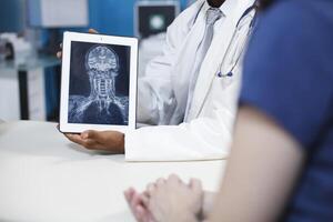 detailopname van röntgenstraal resultaten Aan elektronisch tablet Bij een medisch kantoor. zwart dokter houdt apparaat met radiografie van de hersenen en botten, tonen de aanwezigheid van tumoren of echt ziekten en symptomen. foto