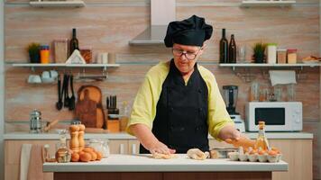 senior vrouw rollend uit de deeg voorbereidingen treffen eigengemaakt brood. gelukkig ouderen chef met bot voorbereidingen treffen rauw ingrediënten naar bakken traditioneel pizza besprenkelen, zeven meel Aan tafel in de keuken. foto