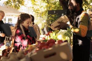 gelukkig meisje ruiken divers eco appels Bij biologisch kruidenier staan met Afrikaanse Amerikaans verkoper, genieten van natuurlijk oogst. vrouw buying vers plaatselijk gegroeid fruit en groenten buiten. foto