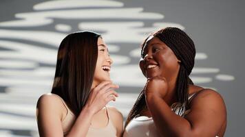 Afrikaanse Amerikaans model- fluisteren geheim met vriend, creëren huidsverzorging en vrouwelijkheid campagne. reclame lichaam positiviteit en zelf liefde in studio, verschillend Dames lachend. mooi meisjes. foto