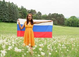 jong vrouw in een geel jurk met de nationaal vlag van Rusland buitenshuis in een bloeiend veld. foto